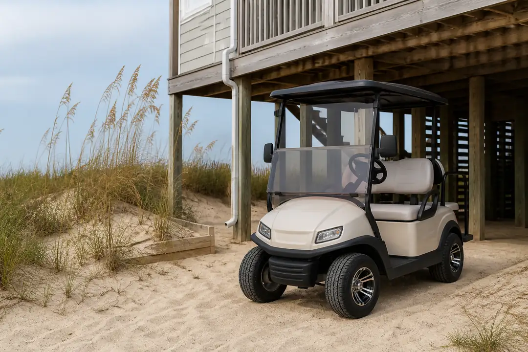 An unbranded golf cart stands beside a raised coastal house and sandy dunes.